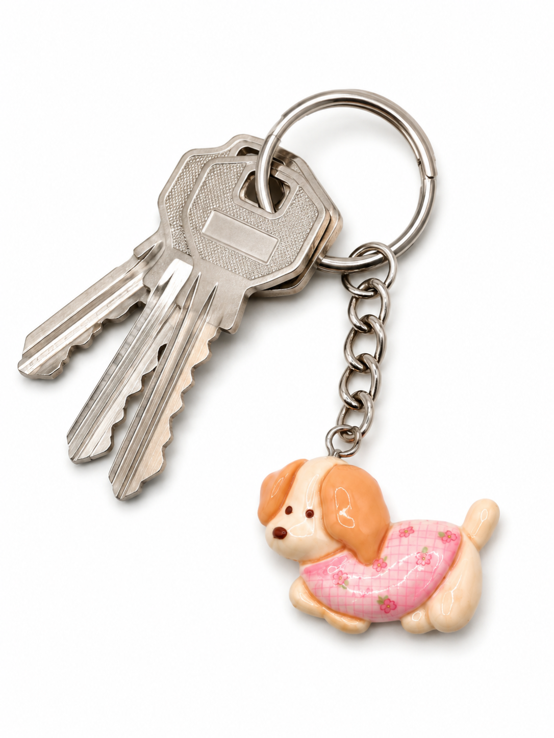 A silver metal keyring with two keys and a small charm shaped like a tan and cream dog wearing a pink patterned diaper, shown on a white background.