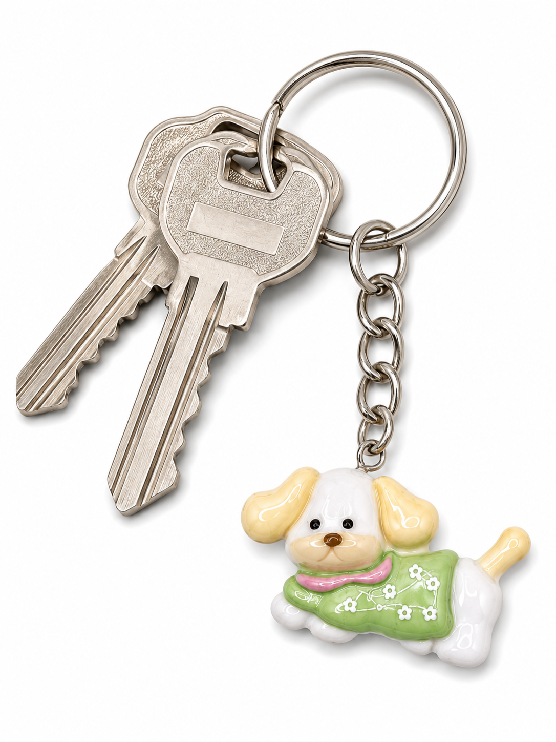 A silver metal keyring with two keys and a dangling ceramic dog keychain. The dog is white with yellow ears, wearing a green dress with white flowers and a pink collar, set against a plain white background.